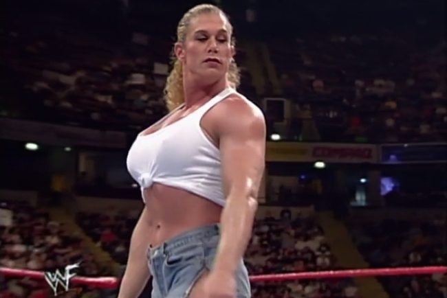 Nicole Bass in 1999, in a white cropped tank top and jeans, standing in the ring