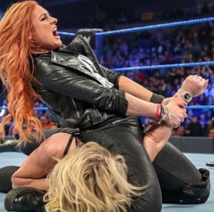 Wrestler Becky Lynch (red-haired woman) doing a submission move on Charlotte Flair (blonde woman).